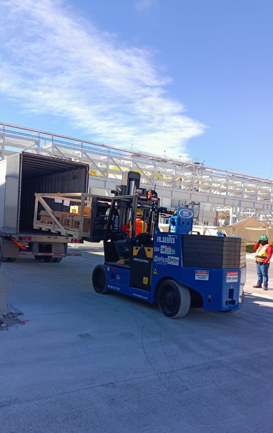 Montacargas el&eacute;ctrico HOIST FR-E 40/60 descargando maquinaria de un tr&aacute;iler en planta